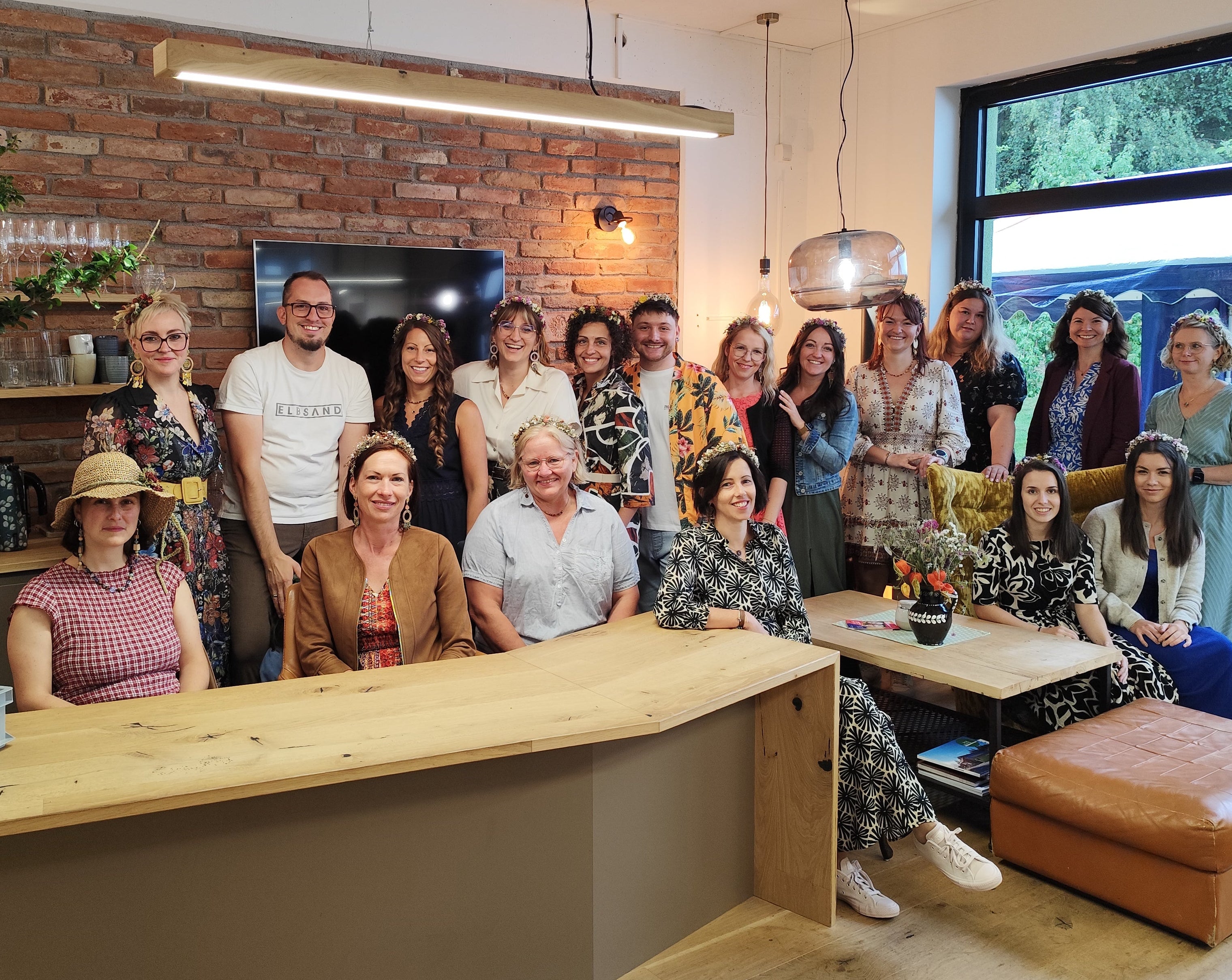 Gruppenfoto des Astwerk Teams beim 10-Jahresfest in einem Innenraum mit Backsteinwand, Holztisch und großer Fensterfront; mehrere Mitarbeitende stehen und sitzen gemeinsam im Raum und blicken in die Kamera.
