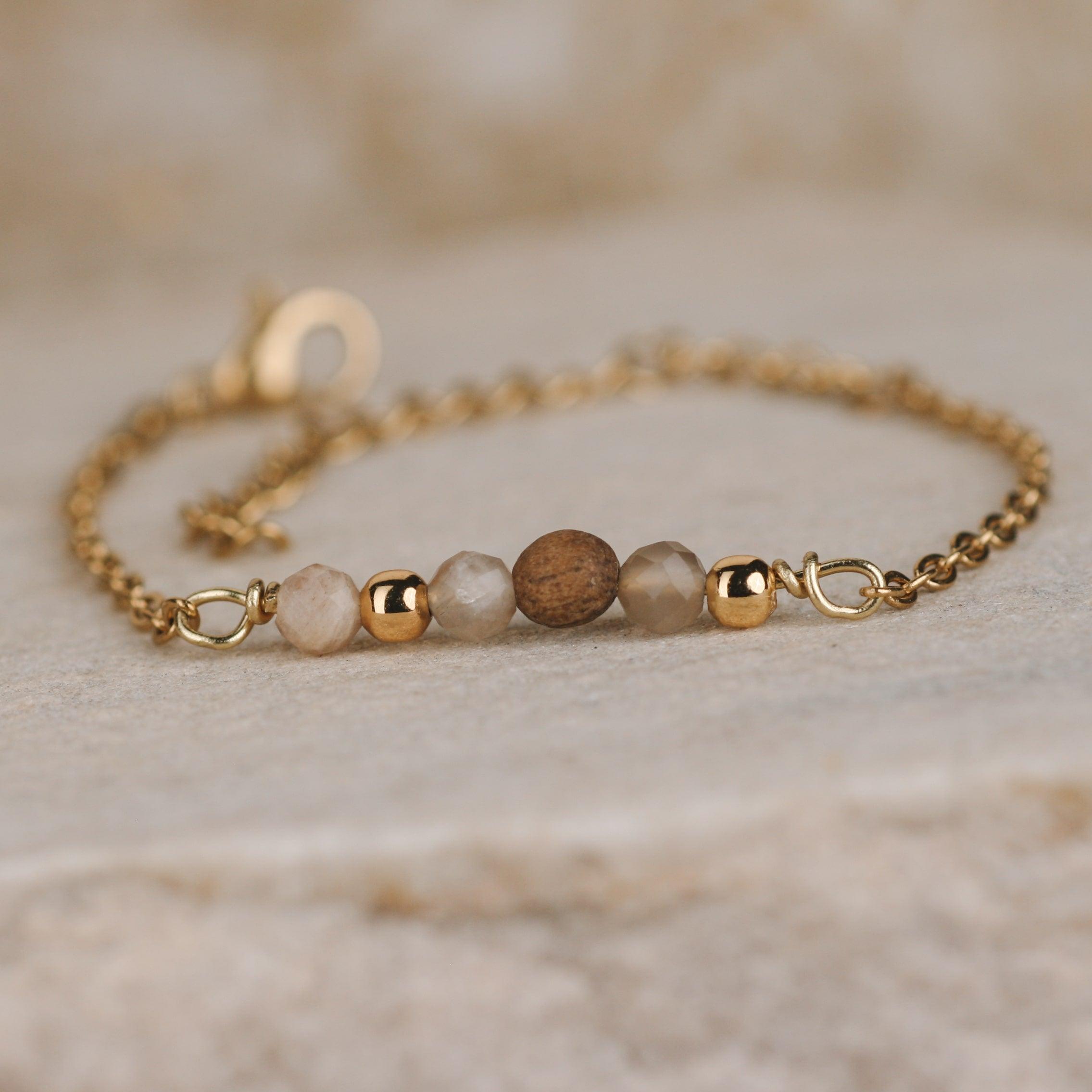 Feines Armband mit Nussholz-Perlen und vergoldeter Edelstahlkette auf hellem Naturstein fotografiert.