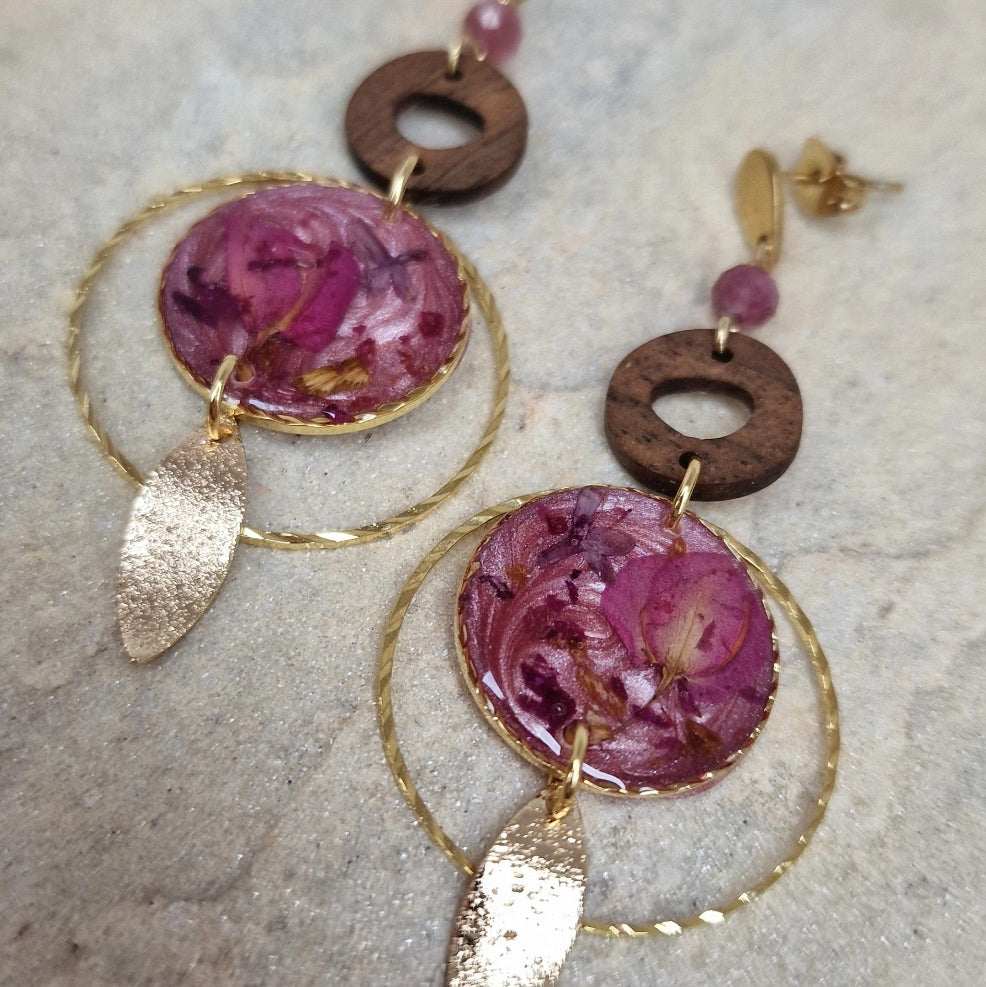 Detailaufnahme von Ohrringen aus Nussholz mit Natursteinen und Resin-Elementen mit echten Blüten, auf hellem Stein arrangiert.