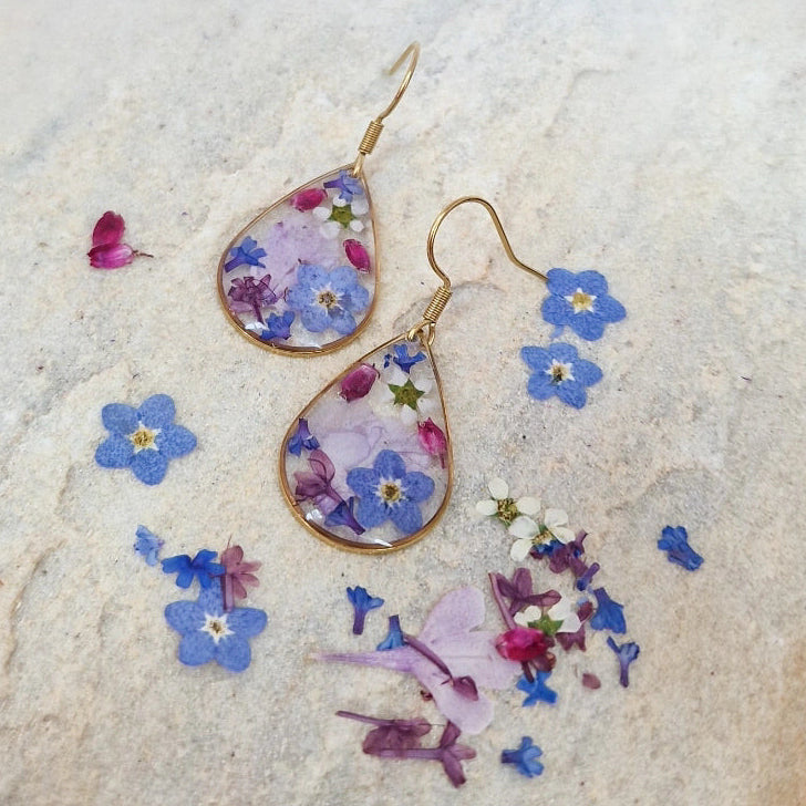 Ohrring mit eigenen Blumen auf hellem Stein und losen Blütenblättern rundherum