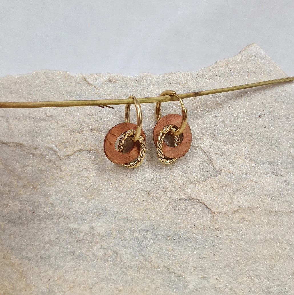 Handgefertigte Kreolen ‚Yara‘ aus Zwetschkenholz und Nussholz mit gewickelten Metallelementen und Edelstahlringen, liegend auf Naturstein