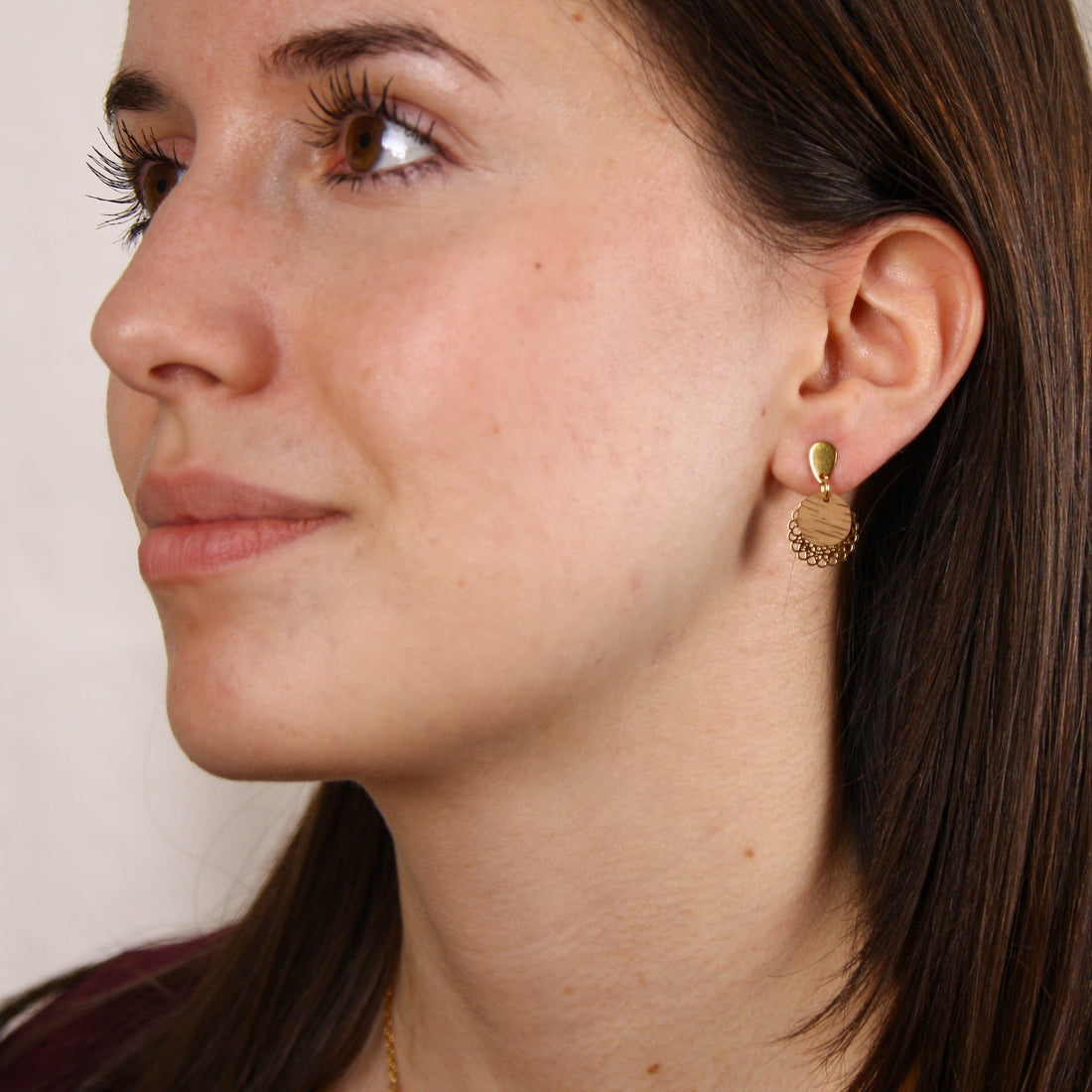 Frau trägt handgefertigte Ohrringe mit runder Nussholzscheibe und goldfarbenem Blumenornament am Ohr.