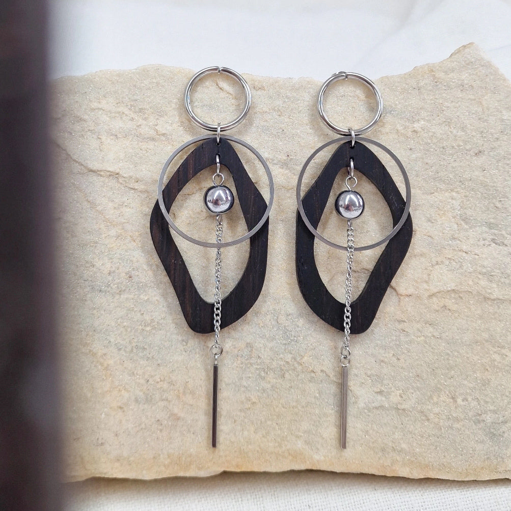 Ohrringe aus dunkler Räuchereiche und silberfarbenen Metall, nebeneinander auf einem hellen Stein arrangiert