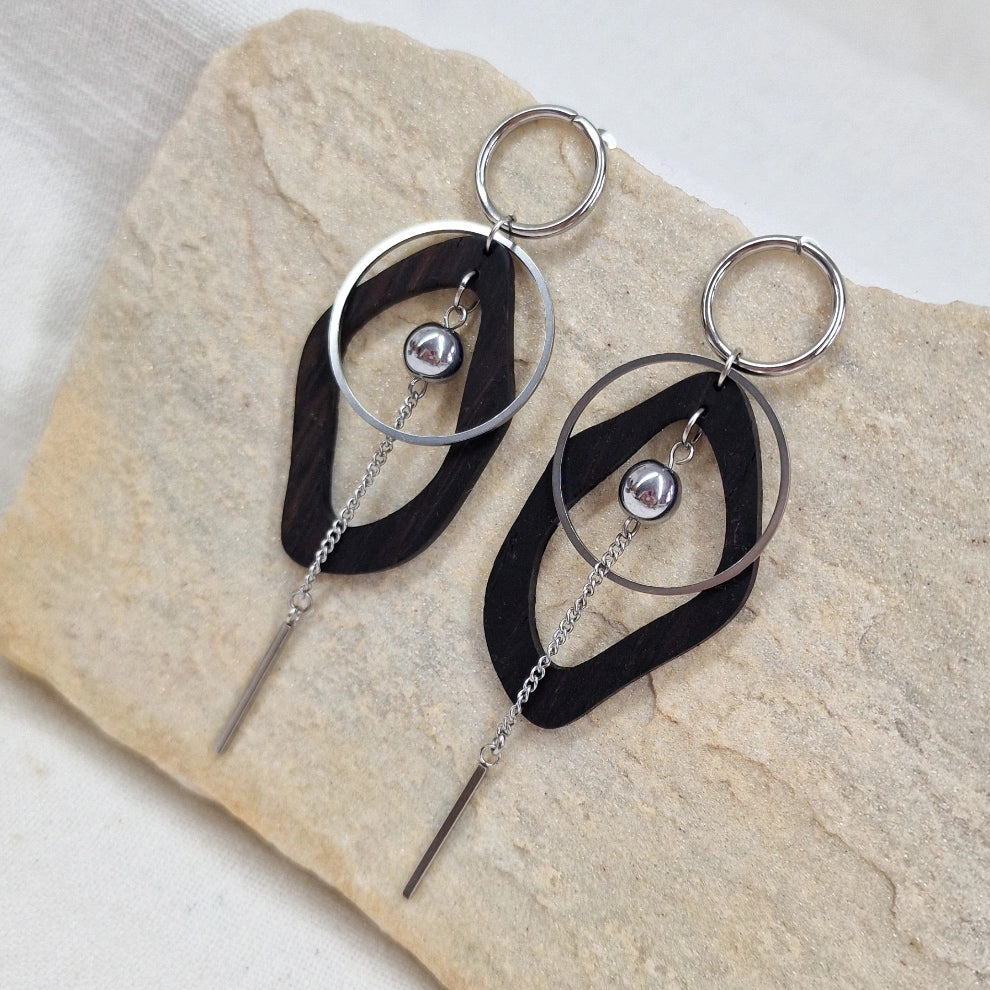 Ohrringe aus dunkler Räuchereiche und silberfarbenen Metall, nebeneinander auf einem hellen Stein arrangiert