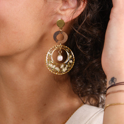Detailansicht der Ohrringe am Ohr, mit Holzring, Resin-Kreis mit weißen Blüten und Blattgold sowie Süßwasserzuchtperle, 6 cm Länge.