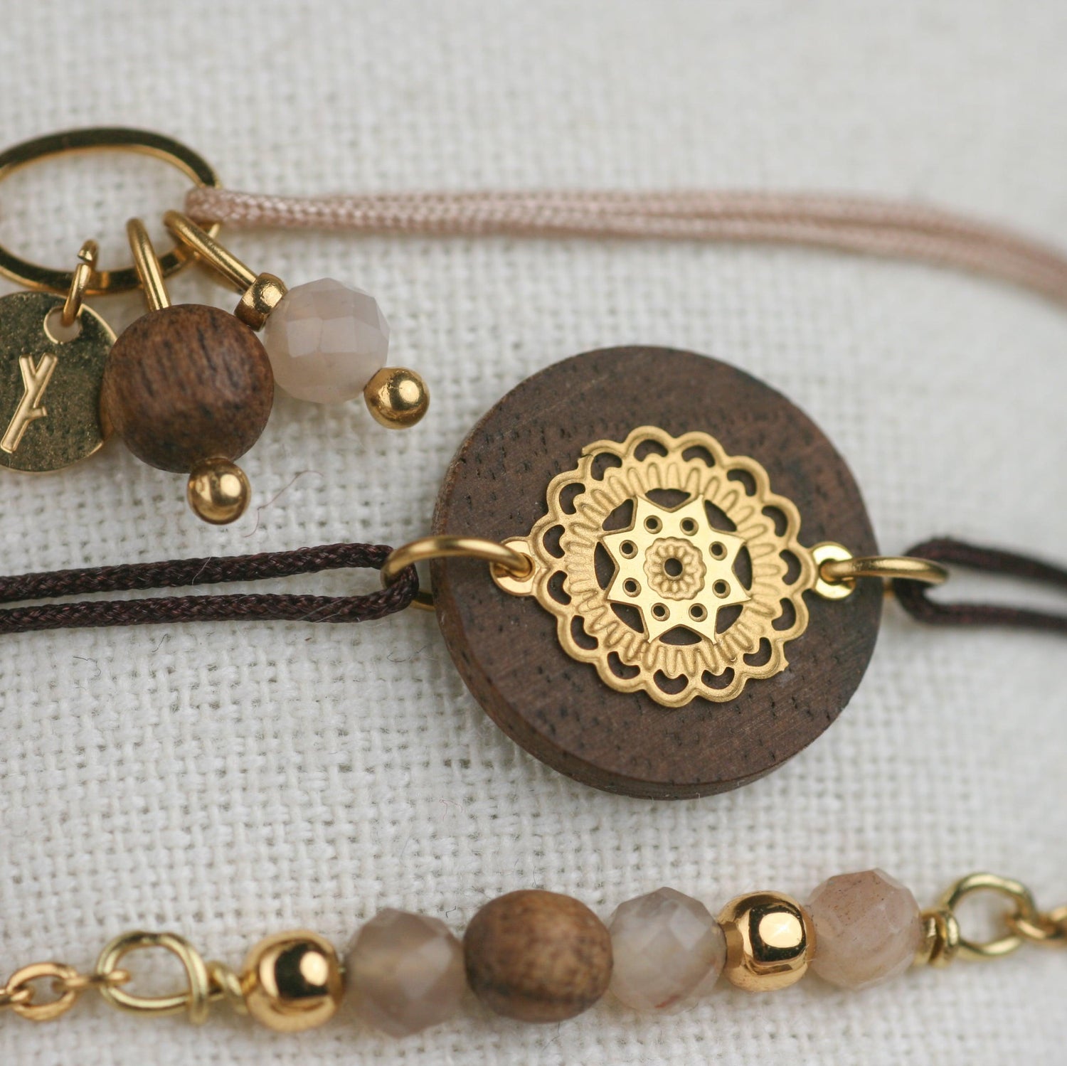 Detailaufnahme eines handgefertigten Armbands mit runder Nussholzscheibe, vergoldetem Ornament und Mondstein auf hellem Untergrund.