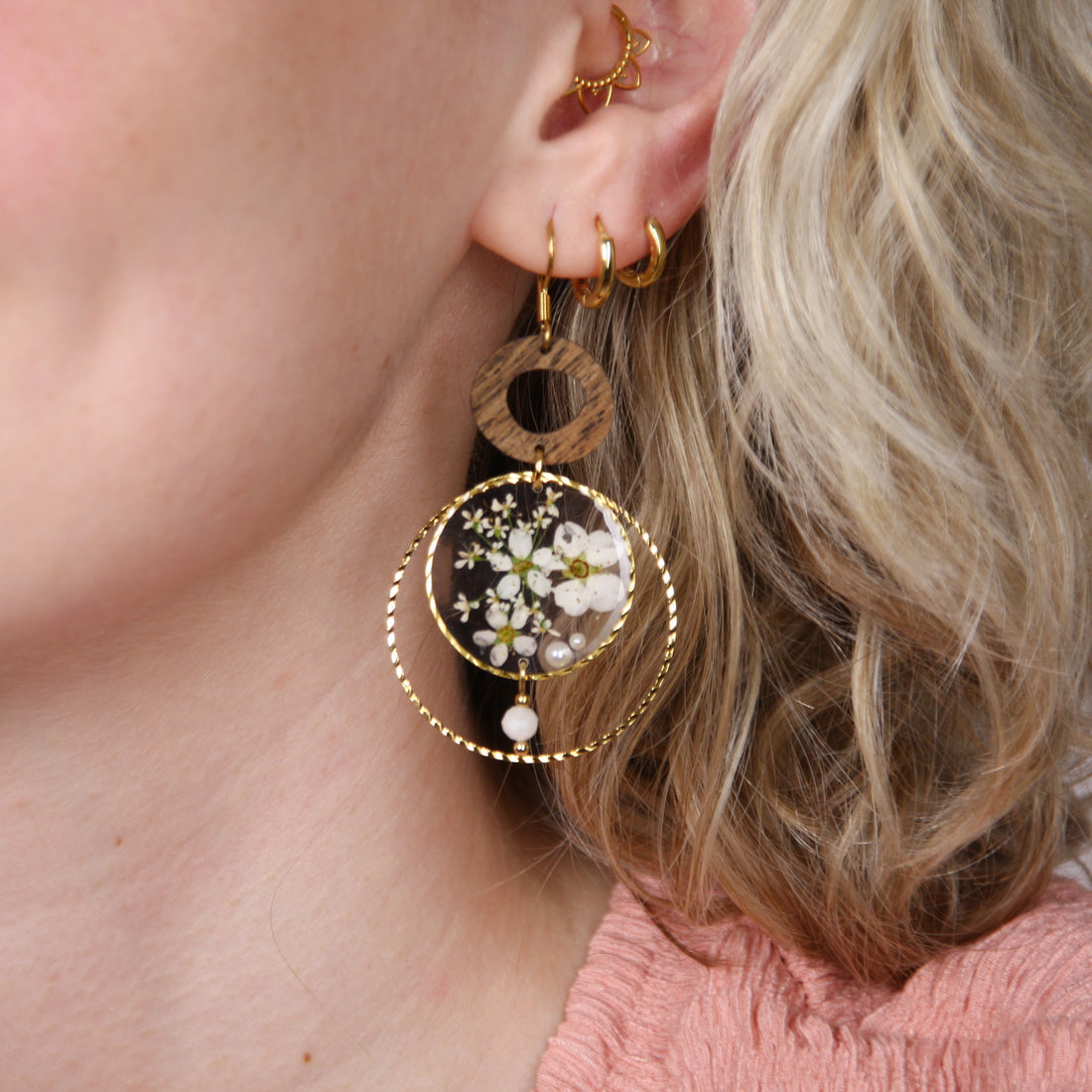 Frau mit kurzen blonden Haaren trägt handgefertigte Holzohrringe aus Nussholz mit transparentem Blumen-Resin, kleiner Perle und silberfarbenem Metallrahmen.