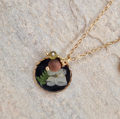 Detailansicht des Anhängers der Halskette ‚Waldlicht‘ aus schwarzem Resin mit echten getrockneten Blüten und Farnen, kombiniert mit Nussholz und Natursteinen