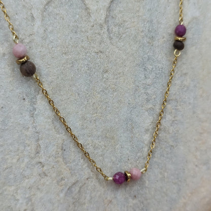 Halskette mit kleinen Nussperlen und farbigen Natursteinen an feiner, goldener Metallkette, liegend auf hellem Stein. Detailaufnahme