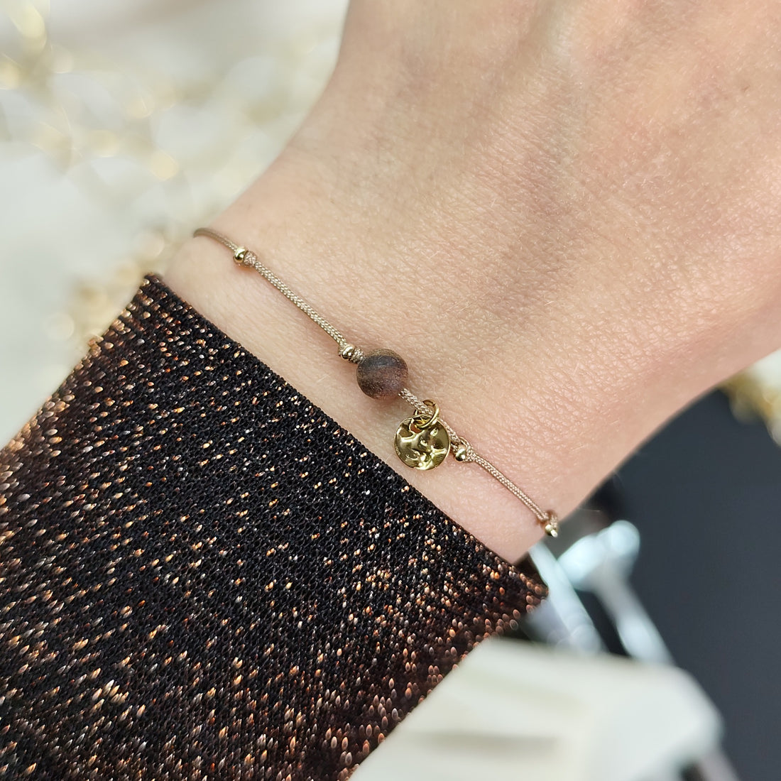 Selbstgemachtes, am Handgelenk getragenes, goldenes Glücksarmband mit Nussholzperle und Edelstahlplättchen auf größenverstellbarem Baumwollband