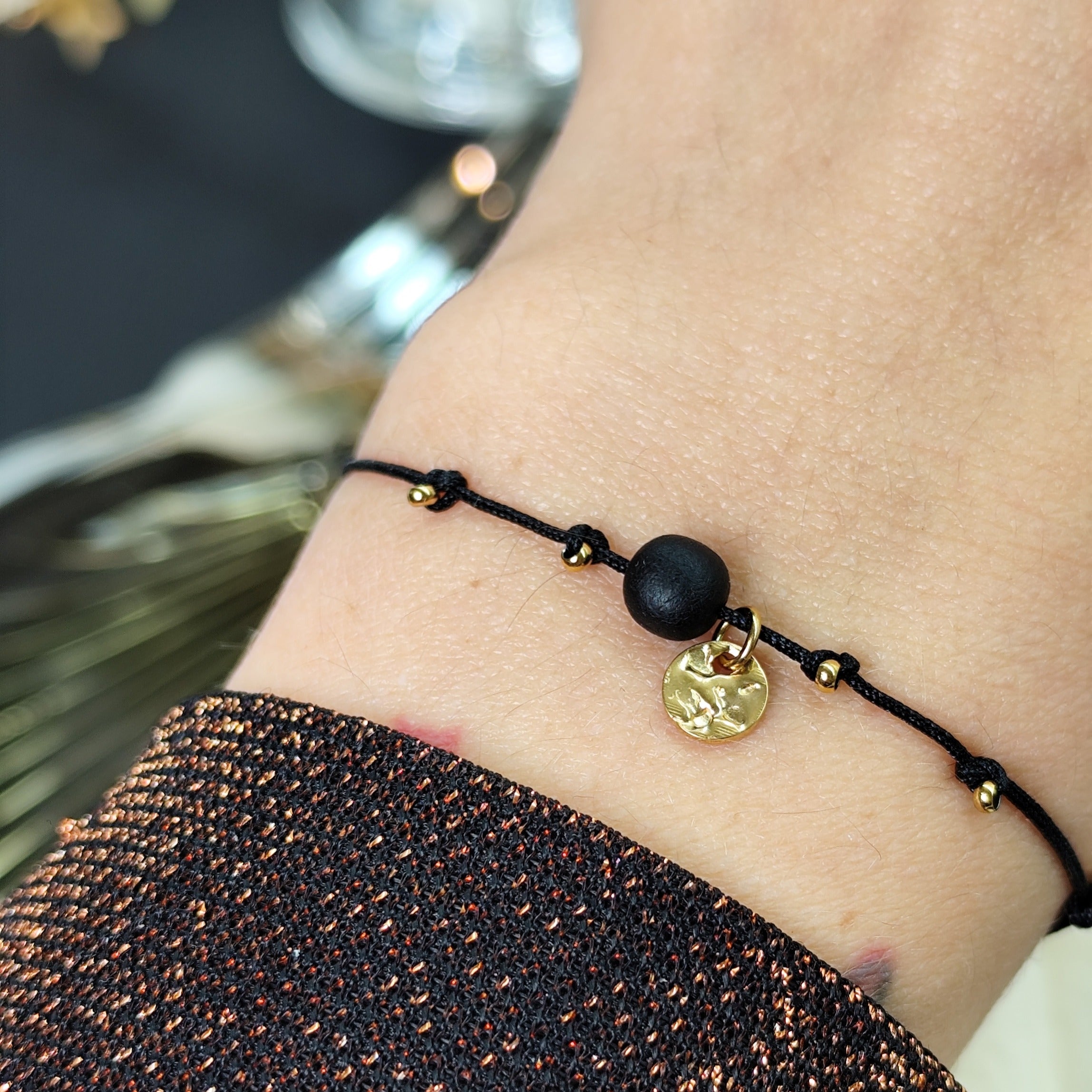 Am Handgelenk getragenes Glücksarmband mit Räuchereicheperle und  goldenen Edelstahlplättchen auf größenverstellbarem Baumwollband