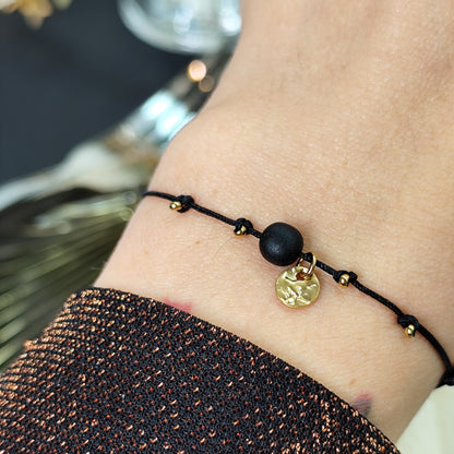 Am Handgelenk getragenes Glücksarmband mit Räuchereicheperle und  goldenen Edelstahlplättchen auf größenverstellbarem Baumwollband