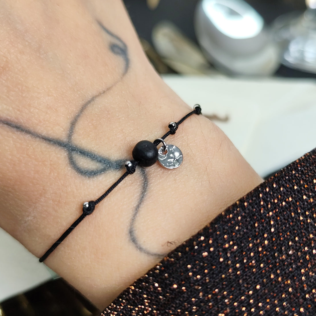 Am Handgelenk getragenes Glücksarmband mit Räuchereicheperle und  silbernen Edelstahlplättchen auf größenverstellbarem Baumwollband
