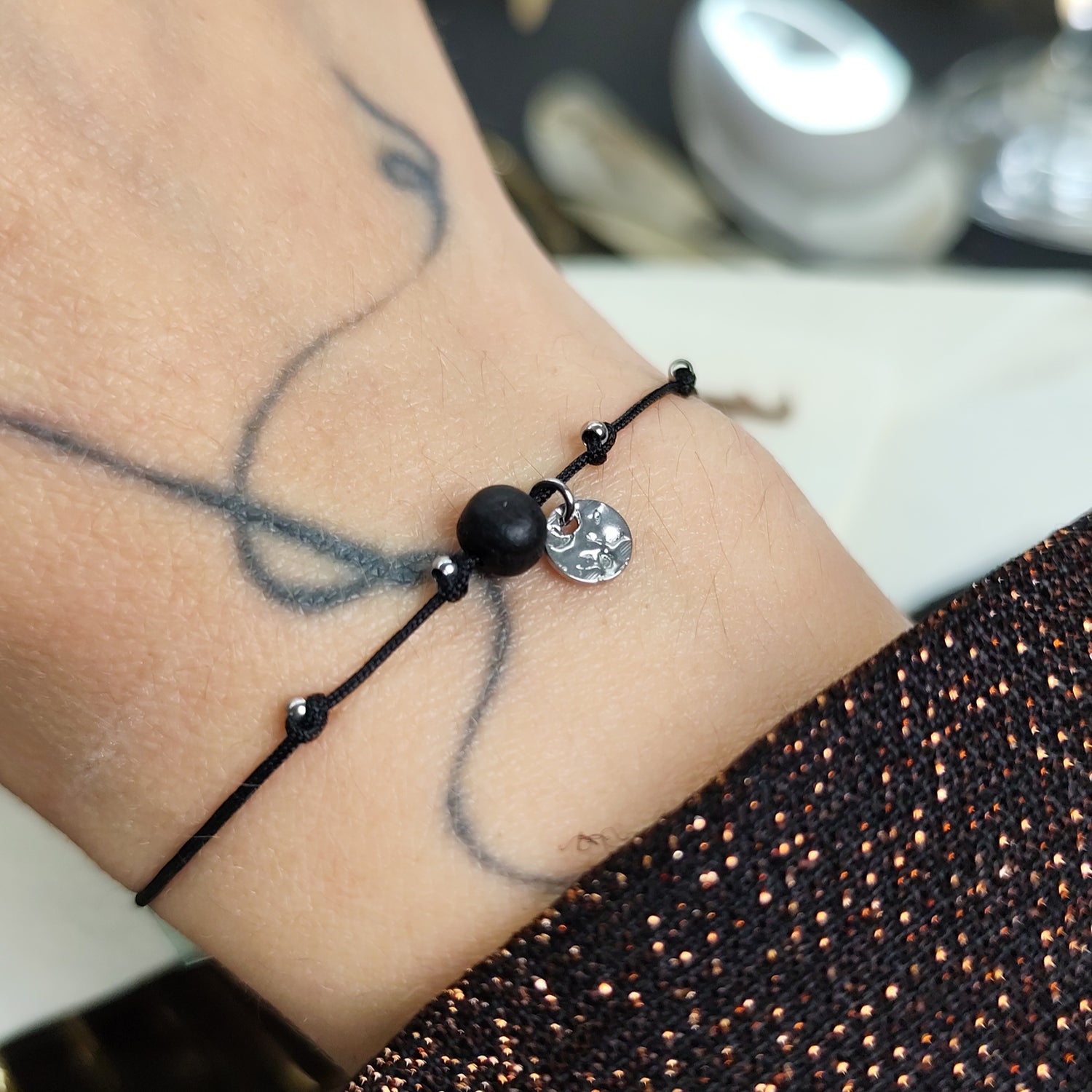 Am Handgelenk getragenes Glücksarmband mit Räuchereicheperle und  silbernen Edelstahlplättchen auf größenverstellbarem Baumwollband