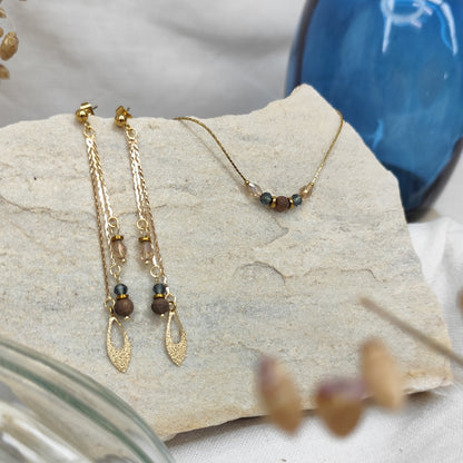 Schmuckset mit Ohrringen und Halskette aus Nussholzperlen, geschliffenen Glaselementen in Blau und Beige sowie Hämatit-Zwischenteilen, liegend auf hellem Stein