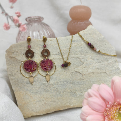 Schmuckset mit Ohrringen, Halskette und Armband aus Nussholz, runden Resin-Elementen mit echten rosa Blüten und goldfarbenen Metallelementen, arrangiert auf hellem Stein mit rosa Blüte im Vordergrund