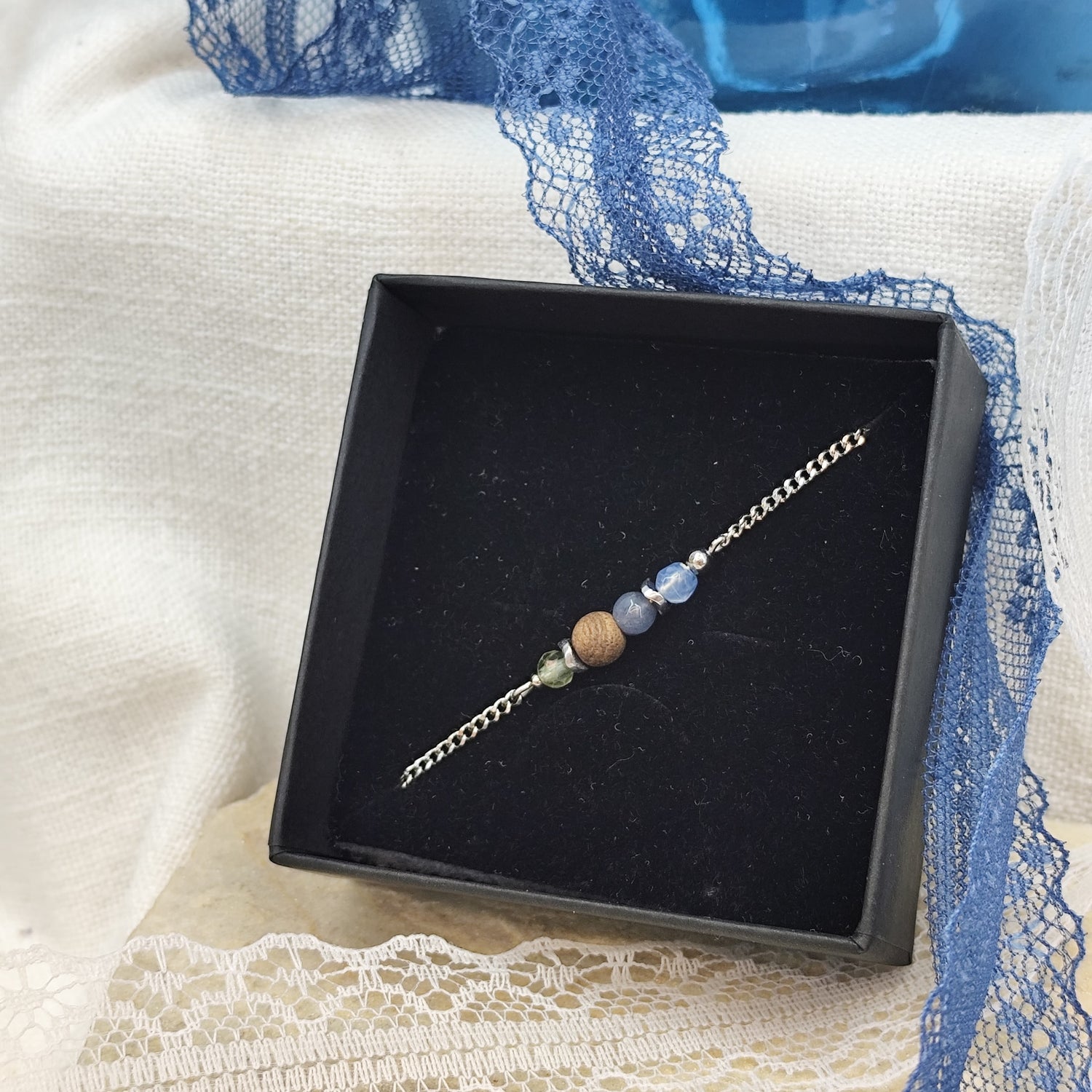 Armband mit blauen und grünen Natursteinen, Nussholzkugel und Hämatit-Zwischenteilen in einer schwarzen Schmuckschachtel