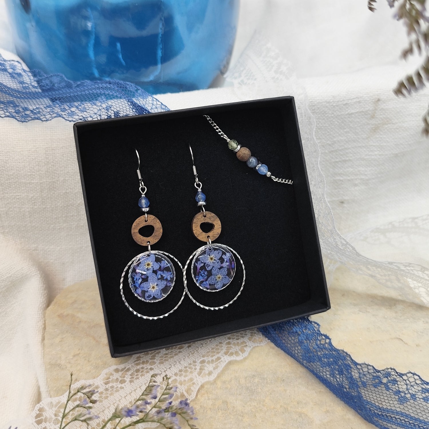 Ohrringe und Armband aus Nussholz mit runden Resin-Elementen und echten Vergissmeinnicht-Blüten, gemeinsam arrangiert in einer schwarzen Samtschachtel. Silber