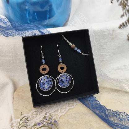 Ohrringe und Armband aus Nussholz mit runden Resin-Elementen und echten Vergissmeinnicht-Blüten, gemeinsam arrangiert in einer schwarzen Samtschachtel. Silber