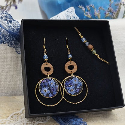 Goldene Ohrringe und Armband aus Nussholz mit runden Resin-Elementen und echten Vergissmeinnicht-Blüten, gemeinsam arrangiert in einer schwarzen Samtschachtel