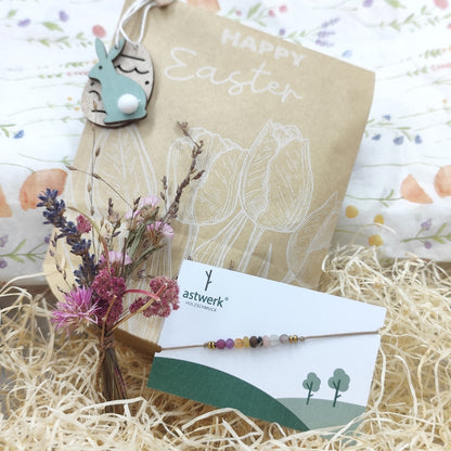 Armband mit Nussperle und farbigen Natursteinperlen auf Mischgewebeband neben Schmuckverpackung und getrockneten Blumen dekoriert