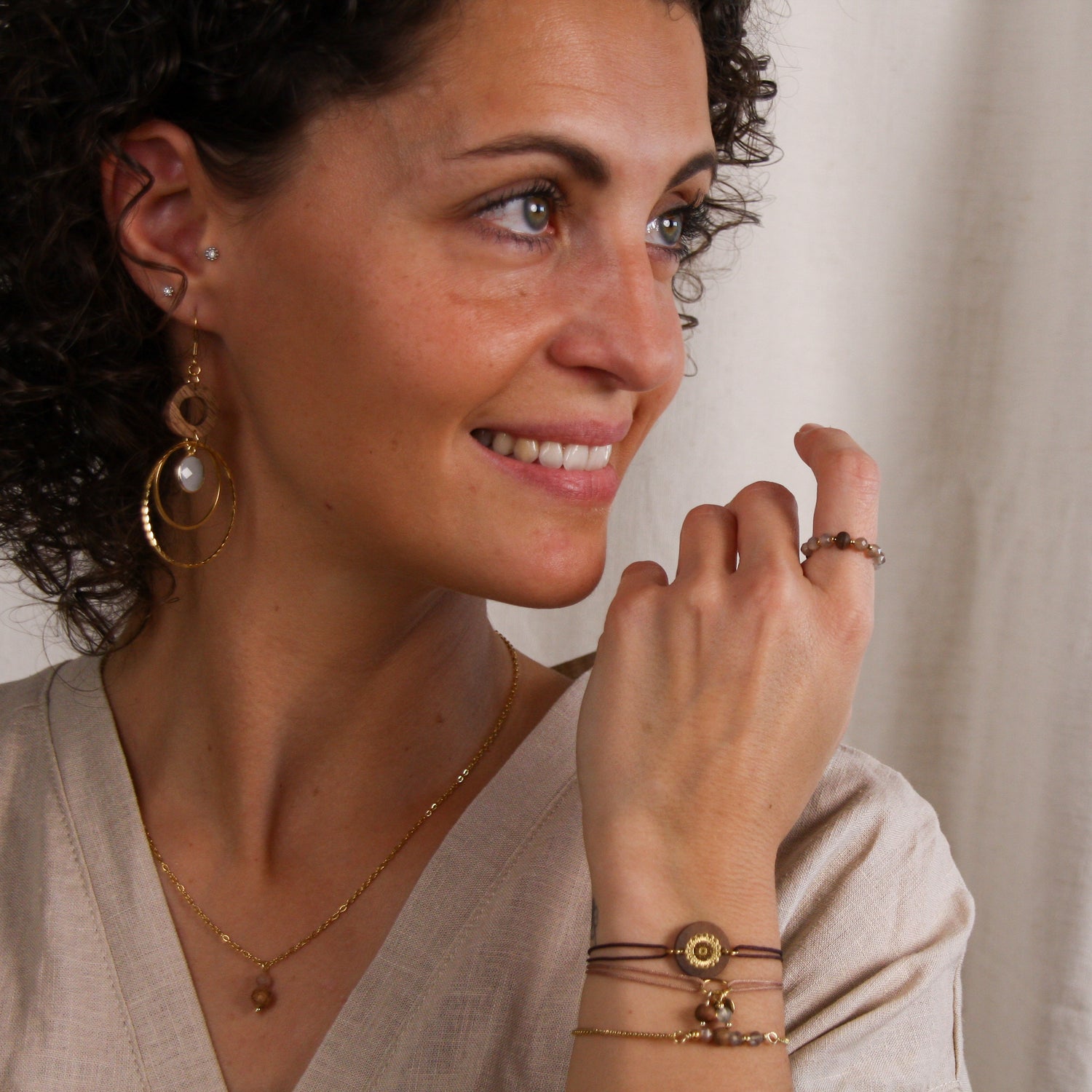 Frau trägt das Schmuckset ‚Harmonia‘ mit Ohrringen, Halskette und Armband aus Nussholz, weißem Quarz und goldfarbenen Metallelementen sowie eine kombinierte Harmonia-Armbandkombination am Handgelenk