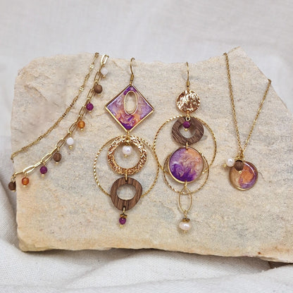 Handgefertigtes Schmuckset aus Nussholz mit goldfarbenem Edelstahl, Resinelement und Natursteinen, bestehend aus Ohrringen, Halskette und Armband, arrangiert auf hellem Stein