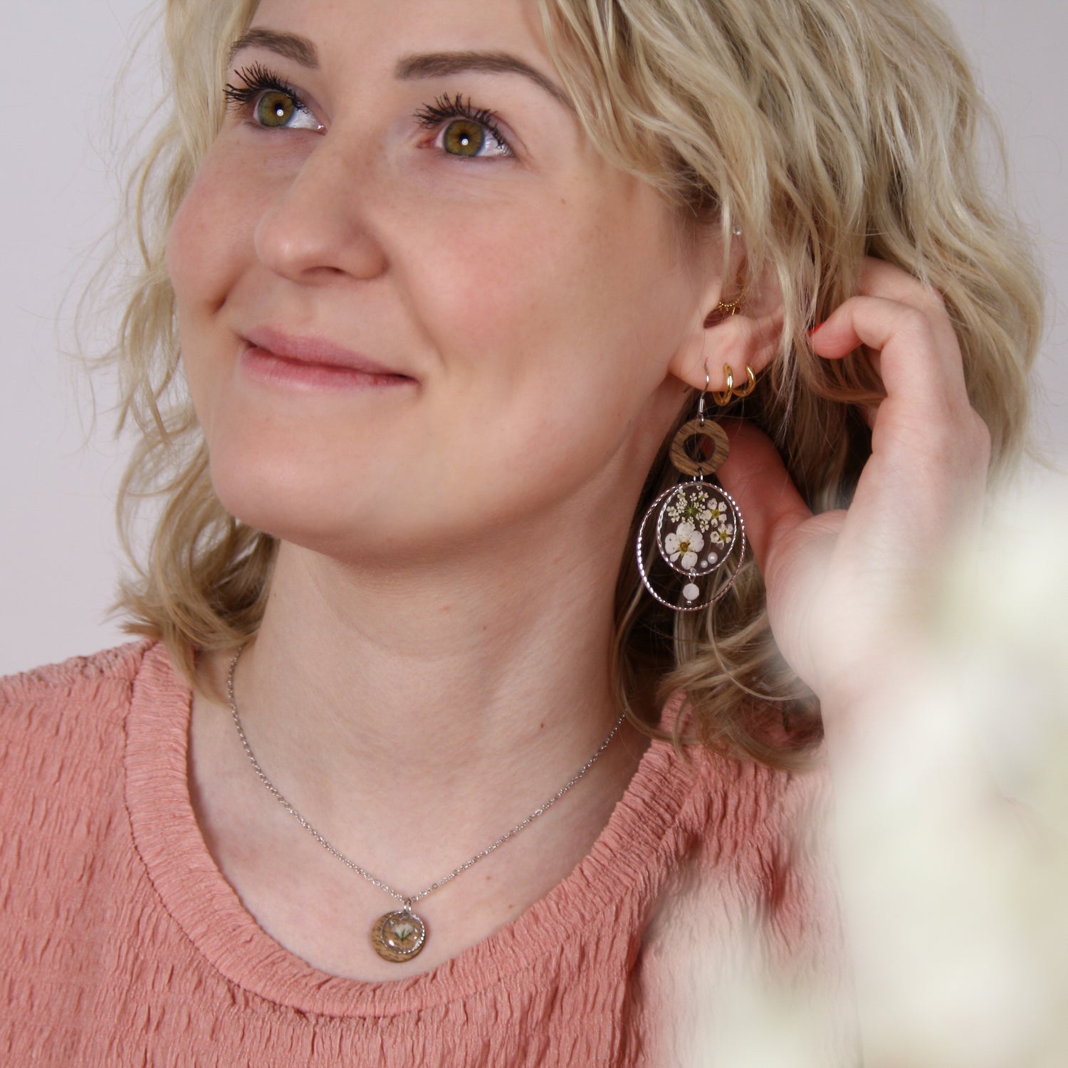 Nahaufnahme einer Frau mit handgefertigten Holzohrringen aus Nussholz, echten Blüten im Resin-Element, kleiner Perle und filigraner Metallfassung.