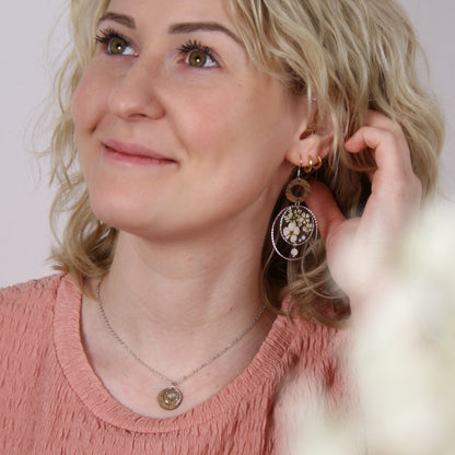 Nahaufnahme einer Frau mit handgefertigten Holzohrringen aus Nussholz, echten Blüten im Resin-Element, kleiner Perle und filigraner Metallfassung.