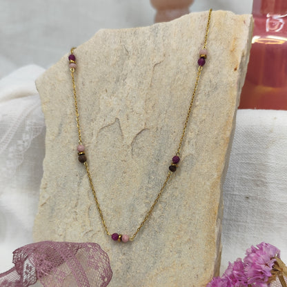 Halskette mit kleinen Nussperlen und farbigen Natursteinen an feiner, goldener Metallkette, liegend auf hellem Stein