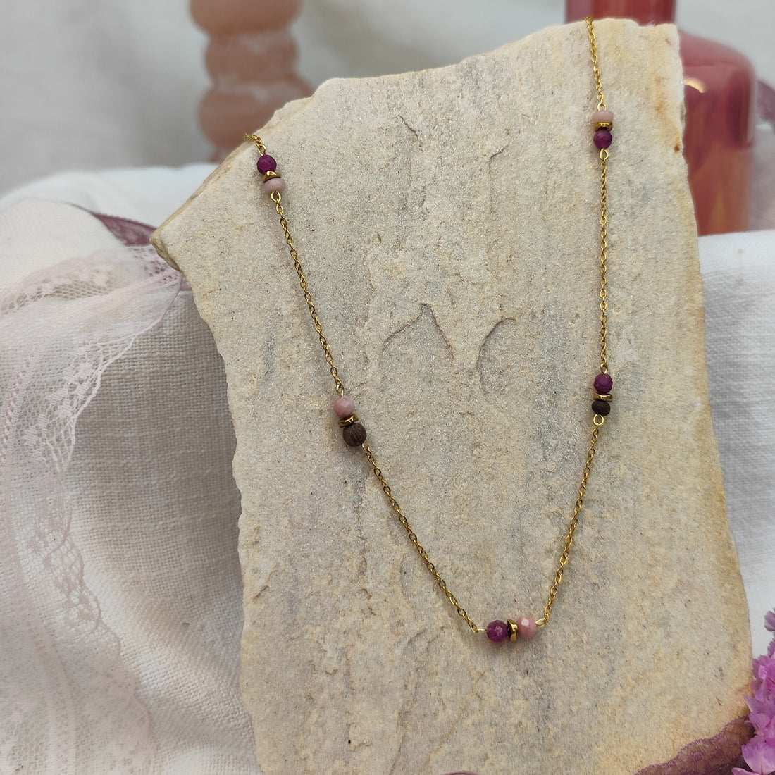 Halskette mit kleinen Nussperlen und farbigen Natursteinen an feiner, goldener Metallkette, liegend auf hellem Stein