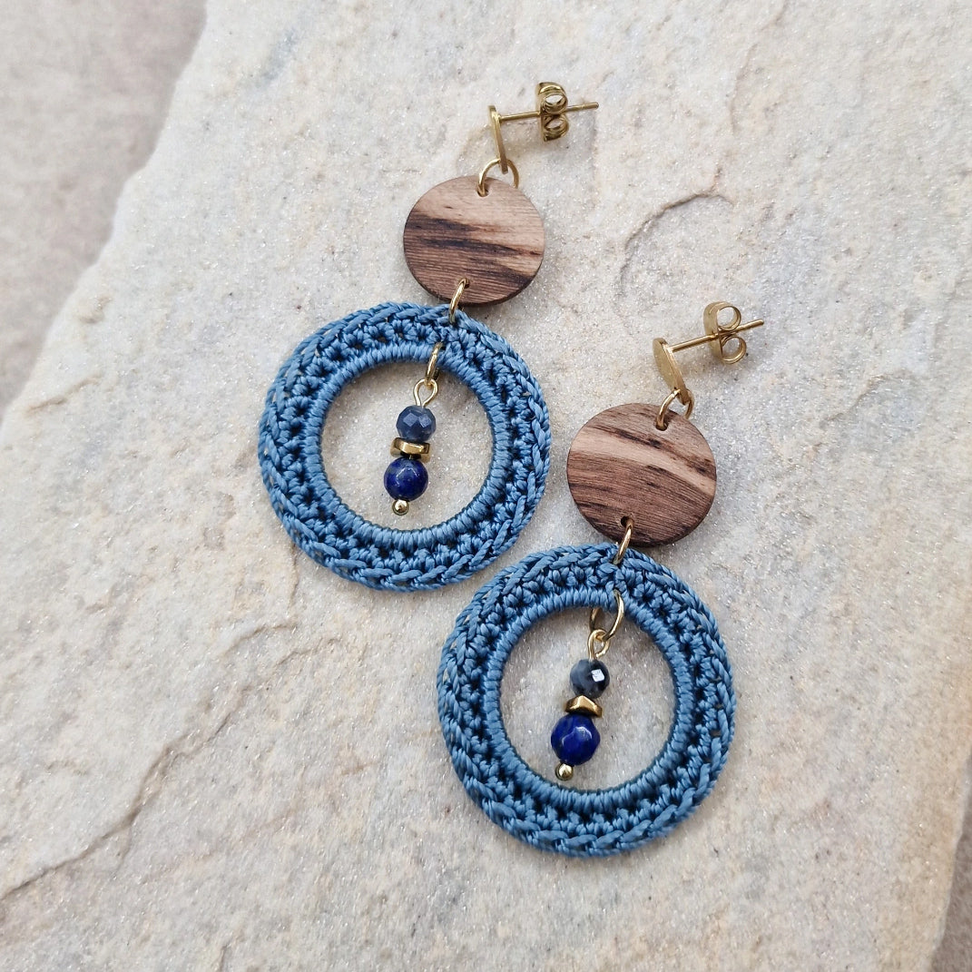 Paar Ohrringe mit Weinstockholz, gehäkelten blauen Ringen und Natursteinperlen auf hellem Steinuntergrund