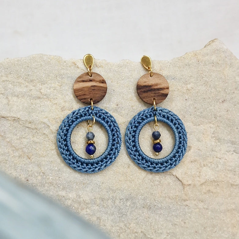 Handgefertigte Ohrringe mit runder Scheibe aus Weinstockholz und gehäkelten Ringen in Himmelblau mit Naturstein in der Mitte auf hellem Naturstein
