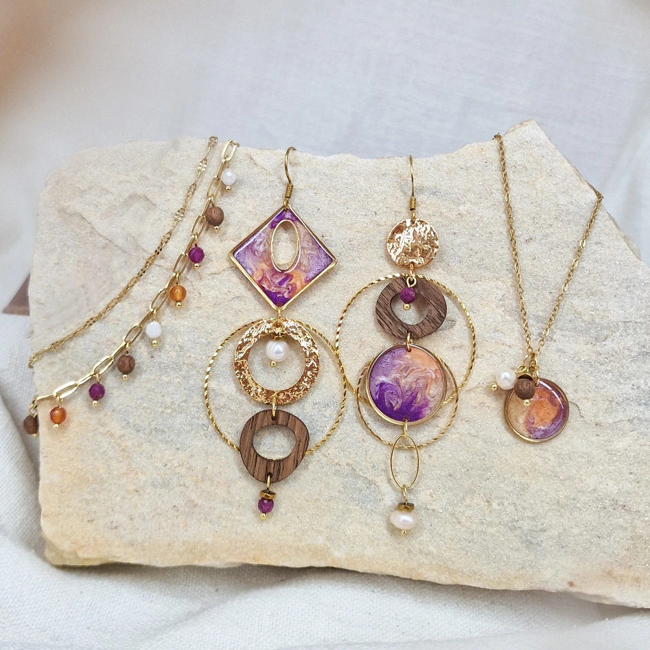 Variation des handgefertigten Holzschmuck-Sets aus Nussholz mit Resinelementen, Natursteinen, Ohrringen, Halskette und Armband, arrangiert auf hellem Naturstein