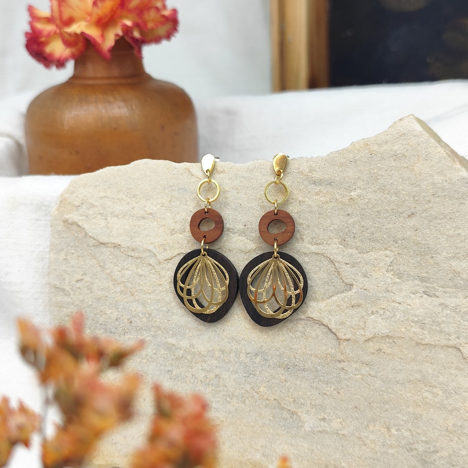 Handgefertigter Holzohrring Zwetschkenzauber auf hellem Naturstein mit orangen Blumen im Vordergrund