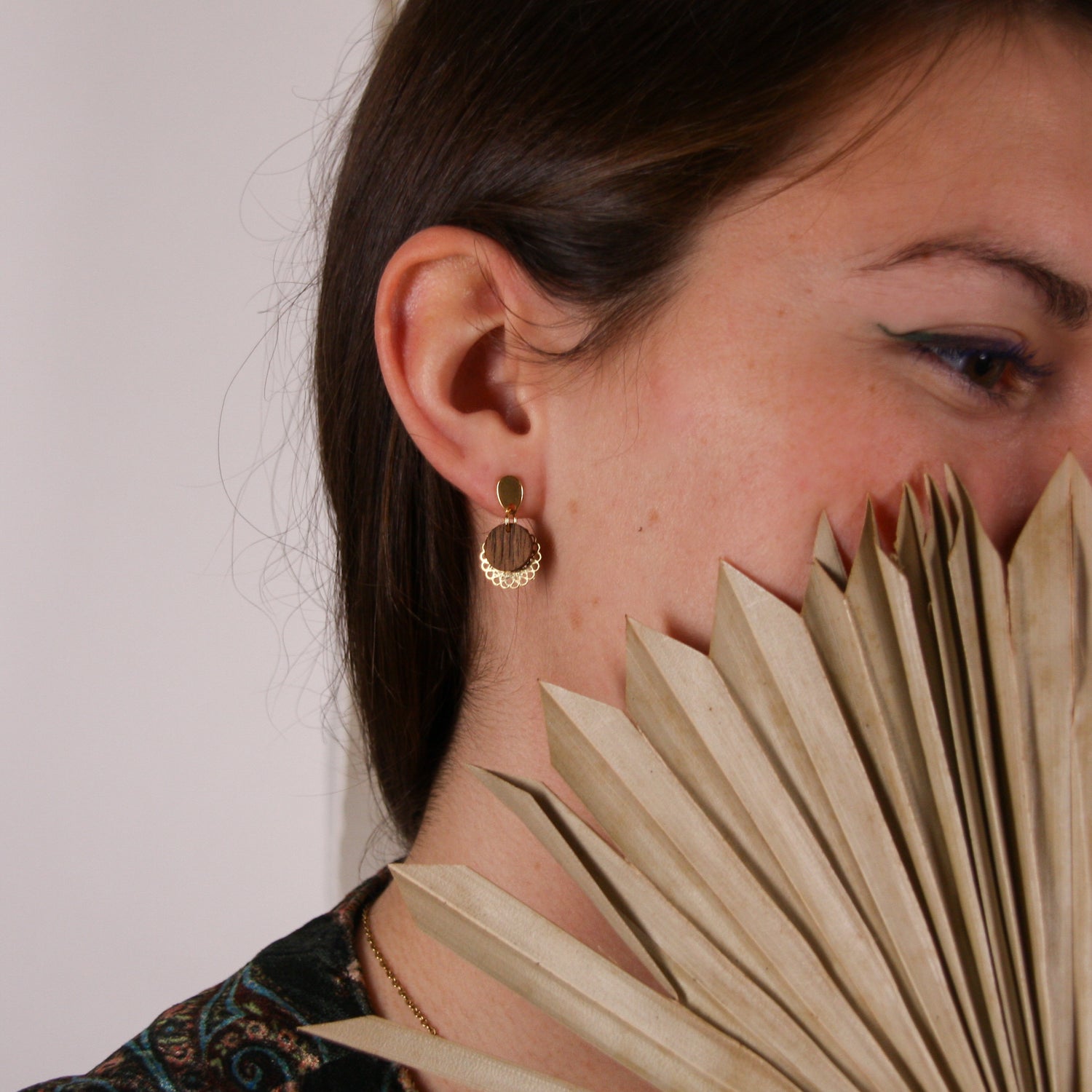 Nahaufnahme einer Frau mit handgefertigten Nussholz-Ohrringen und vergoldetem Blumenornament, kombiniert mit Naturaccessoire.