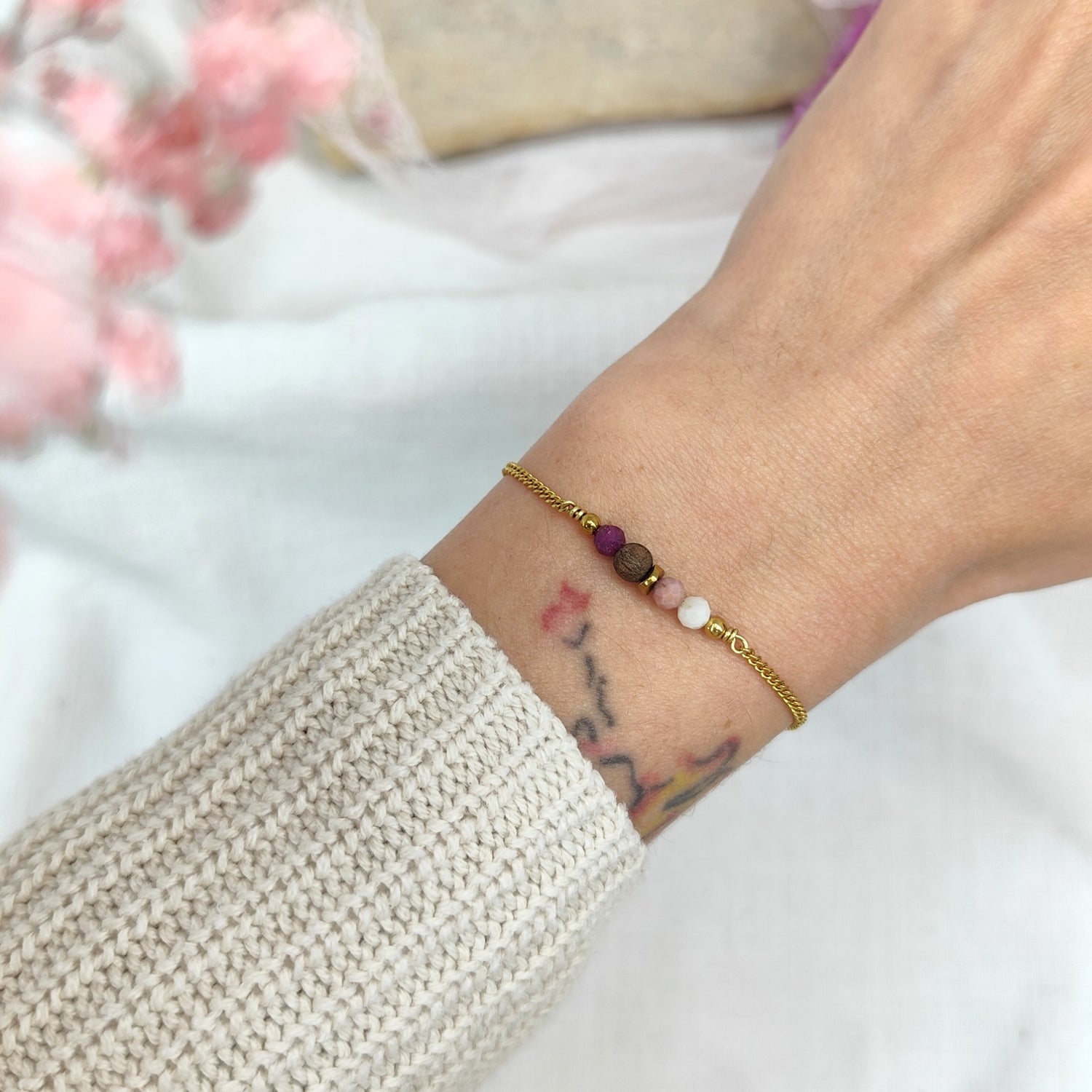 Fein gearbeitetes Armketterl mit rosé- und violettfarbenen Natursteinen an goldener Kette, am Handgelenk getragen
