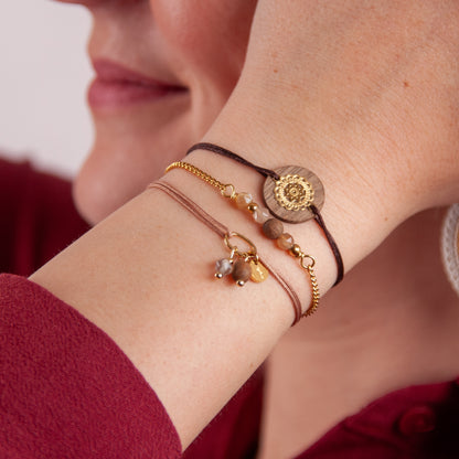 Mehrere handgefertigte Armbänder aus Nussholz und Mondstein kombiniert am Handgelenk, warmes Tageslicht.