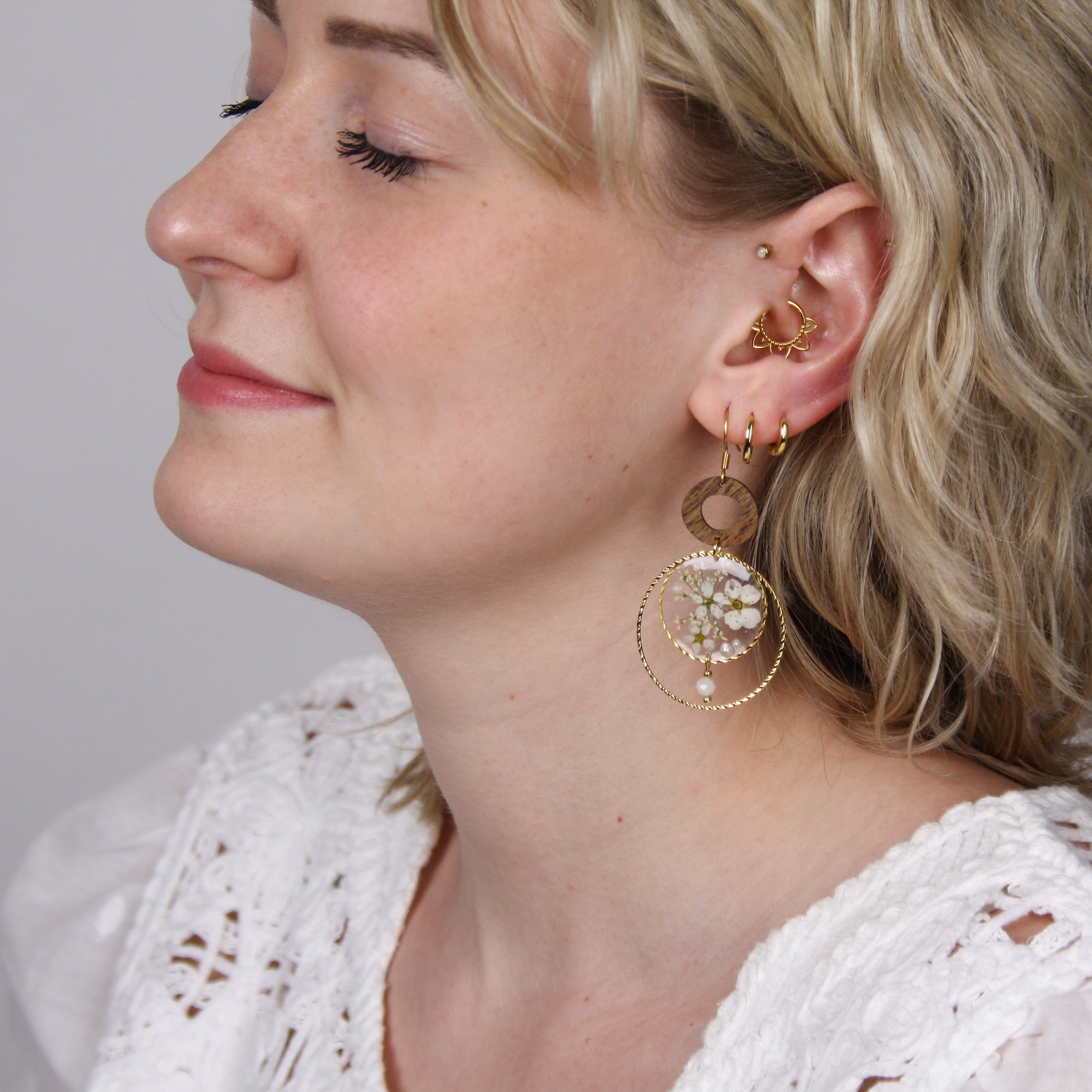 Detailansicht einer Frau mit handgefertigten Ohrringen aus Nussholz und Blumen-Resin, eingefasst in silberfarbenem Metallrahmen mit Perlendetail.