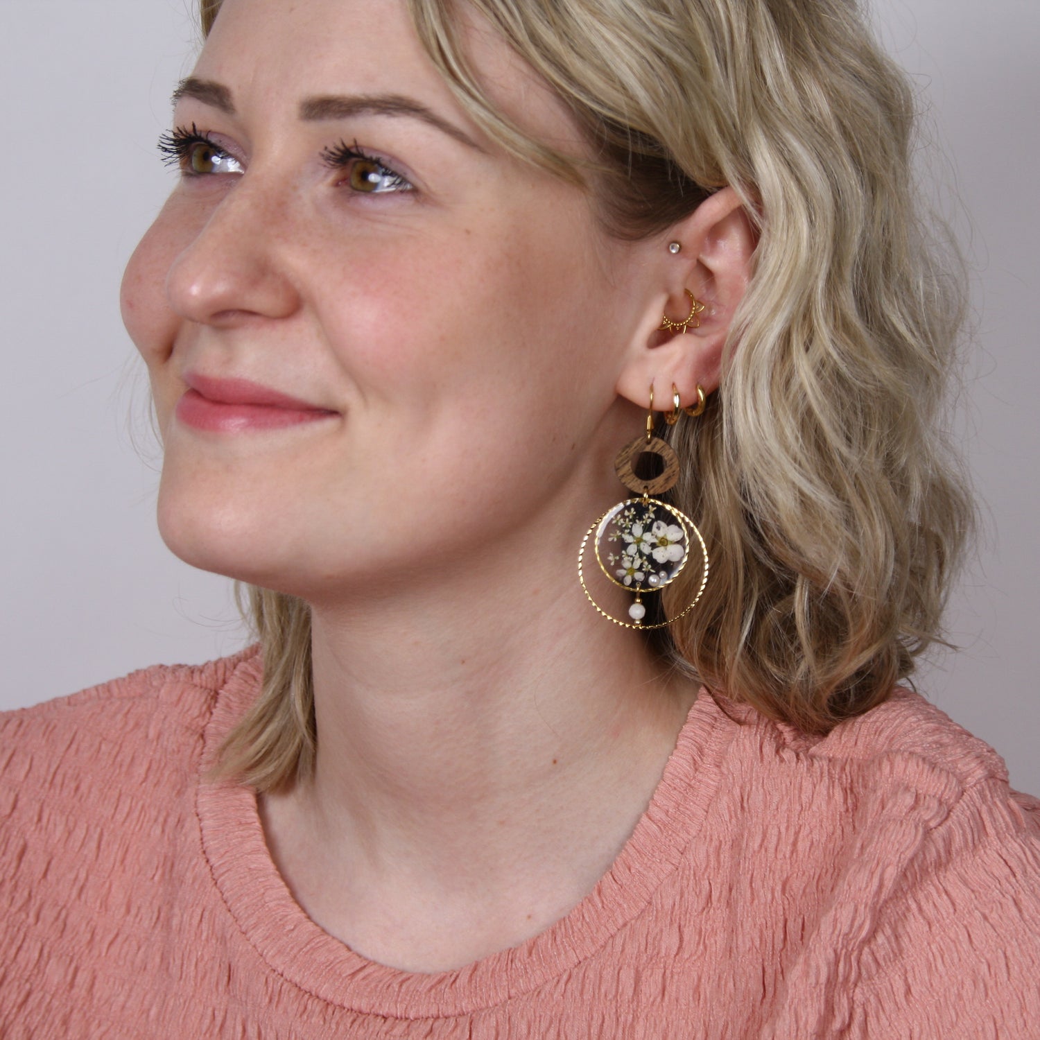Blonde Frau frontal fotografiert mit handgefertigten Holzohrringen aus Nussholz, echten getrockneten Blüten im Resin und kleiner Perle.