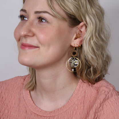 Blonde Frau frontal fotografiert mit handgefertigten Holzohrringen aus Nussholz, echten getrockneten Blüten im Resin und kleiner Perle.