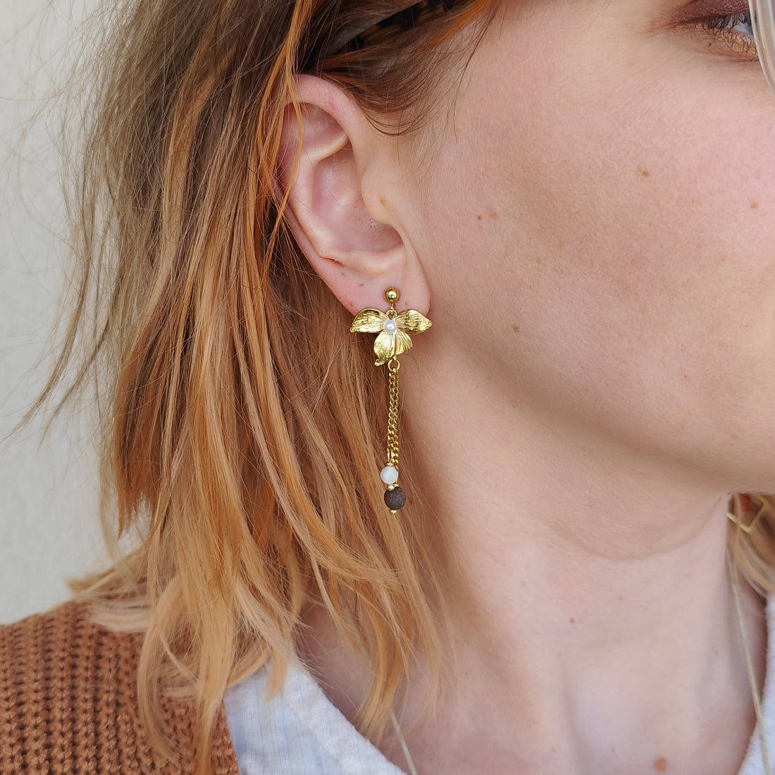 Frau trägt lange goldene Blütenohrringe mit weißem Stein und Nussperle, seitliche Nahaufnahme am Ohr