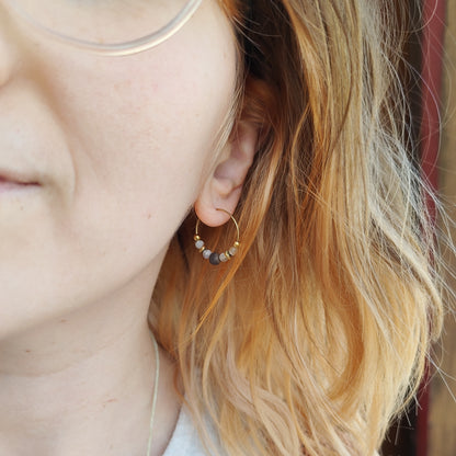 Nahaufnahme eines Ohrs mit eingesetzter Kreole, daran eine runde Mondsteinperle und eine dunklere Nussperle, im Hintergrund helle Kleidung