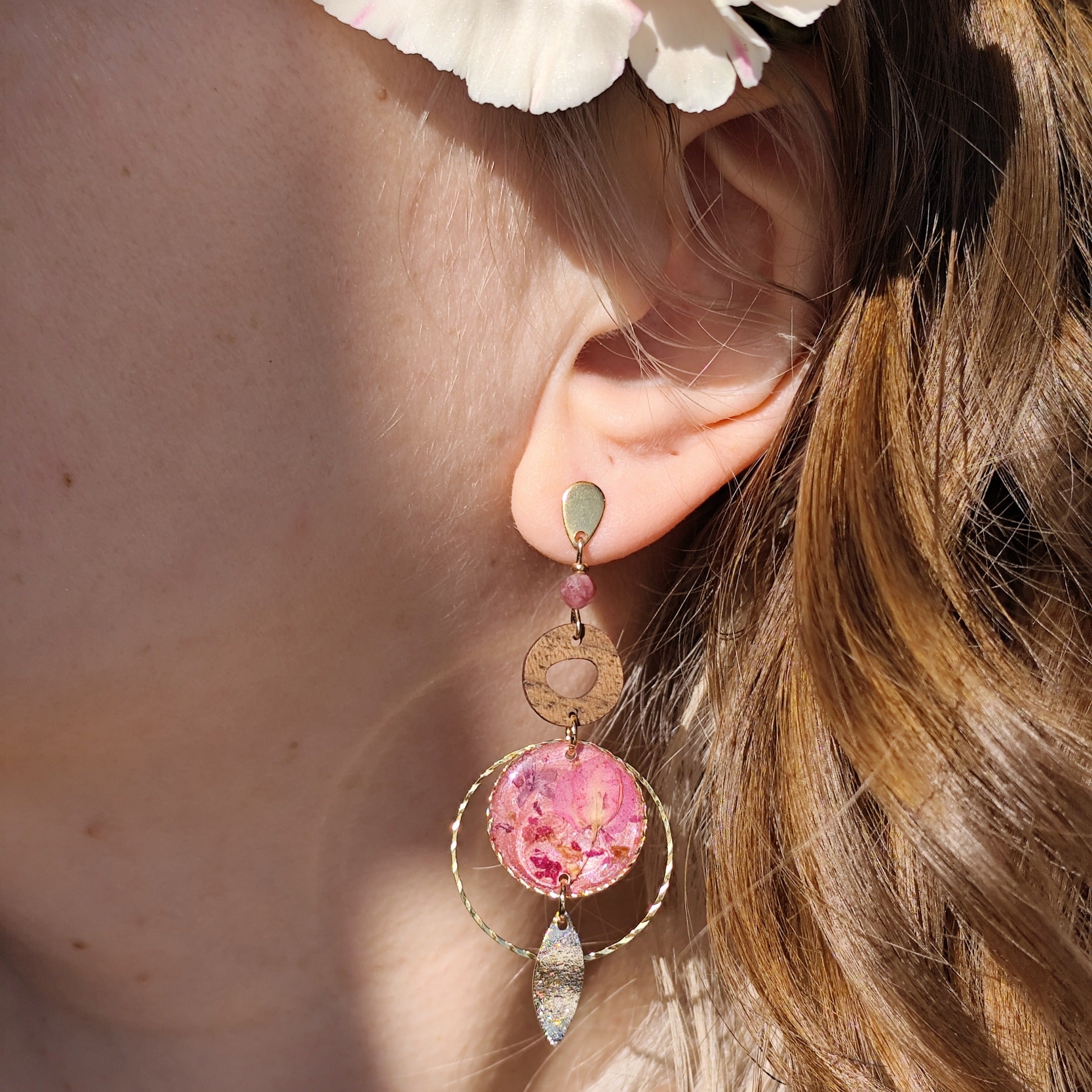 Am Ohr getragener Ohrring aus goldfarbenem Edelstahl mit runder Nussholzscheibe und einem Resin-Element mit echten rosa Blüten, darunter ein filigranes Metallelement