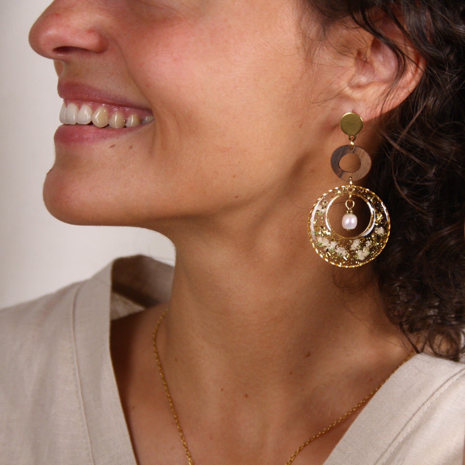 Große runde Ohrringe mit Nussholz-Element und transparentem Resin mit getrockneten Blüten und Blattgold im Profil getragen.