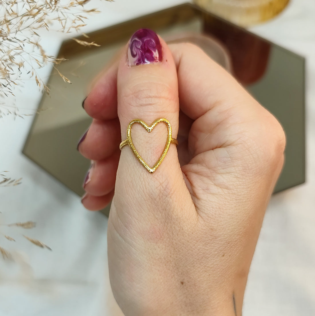 goldener Ring in Herzform auf Daumen mit bunten Nägeln und Spiegel als Hintergrund