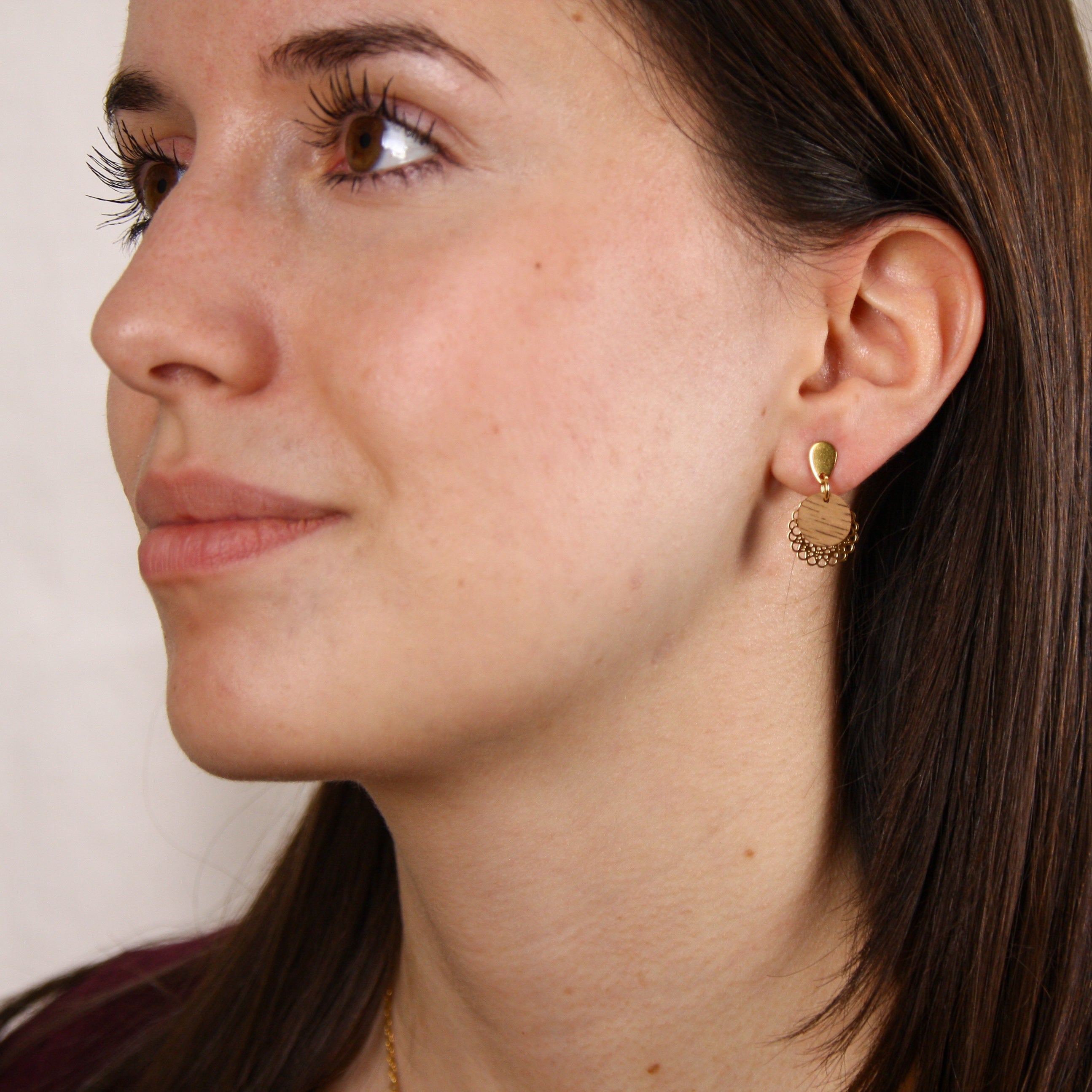 Frau trägt handgefertigte Ohrringe mit runder Nussholzscheibe und goldfarbenem Blumenornament am Ohr.