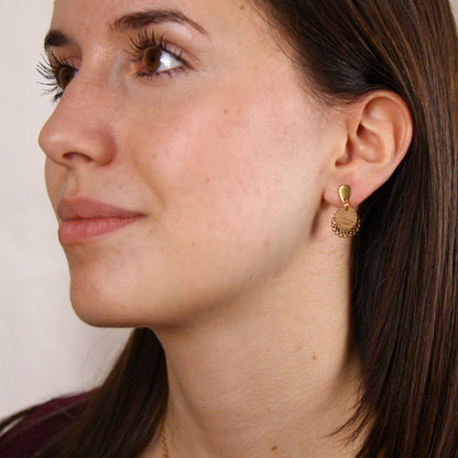 Frau trägt handgefertigte Ohrringe mit runder Nussholzscheibe und goldfarbenem Blumenornament am Ohr.