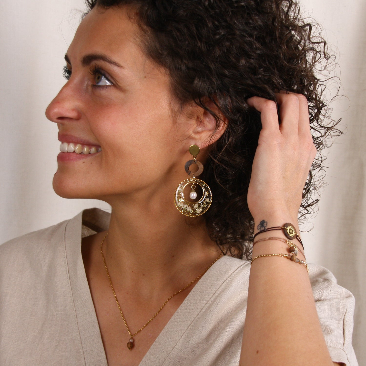 Große runde Ohrringe mit Nussholz-Element und transparentem Resin mit getrockneten Blüten und Blattgold im Profil getragen.