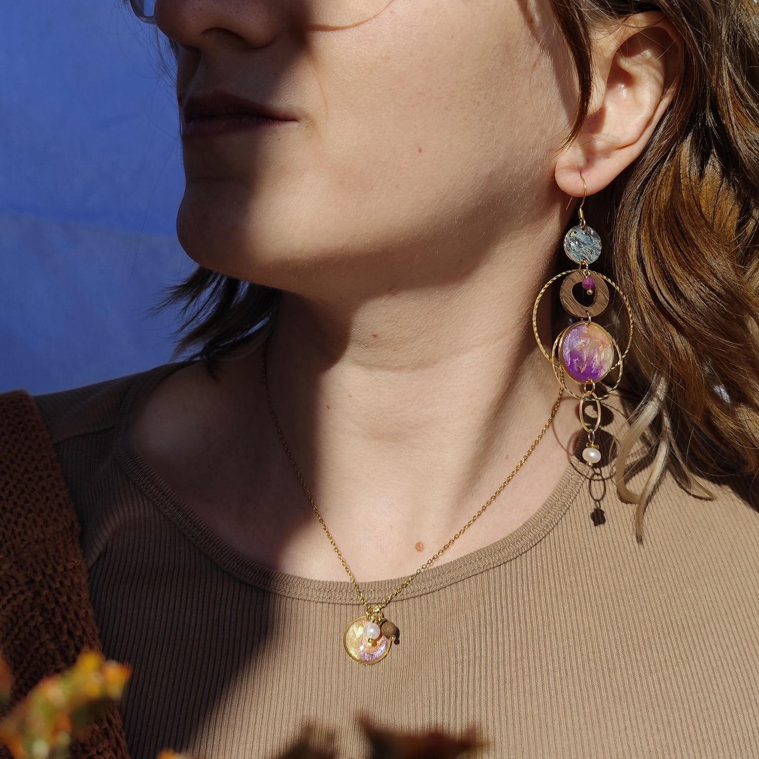 Model trägt handgefertigte Holzohrringe und Halskette aus Nussholz mit goldfarbenen Metallelementen, einem Resinelement und Natursteinen, getragen am Ohr im Profil im Sonnenschein